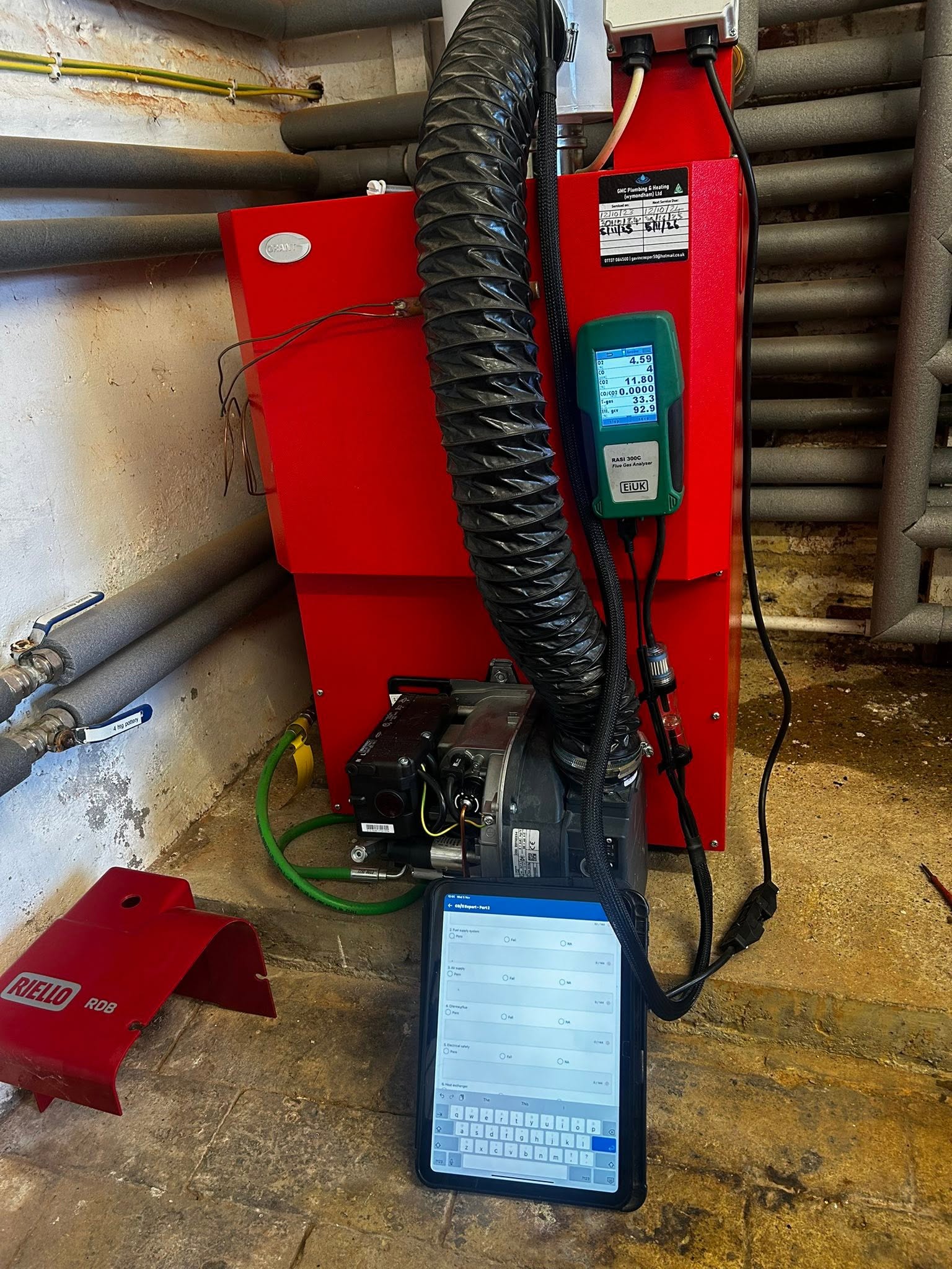 Red oil boiler on test with the analyser and a tablet showing the service record