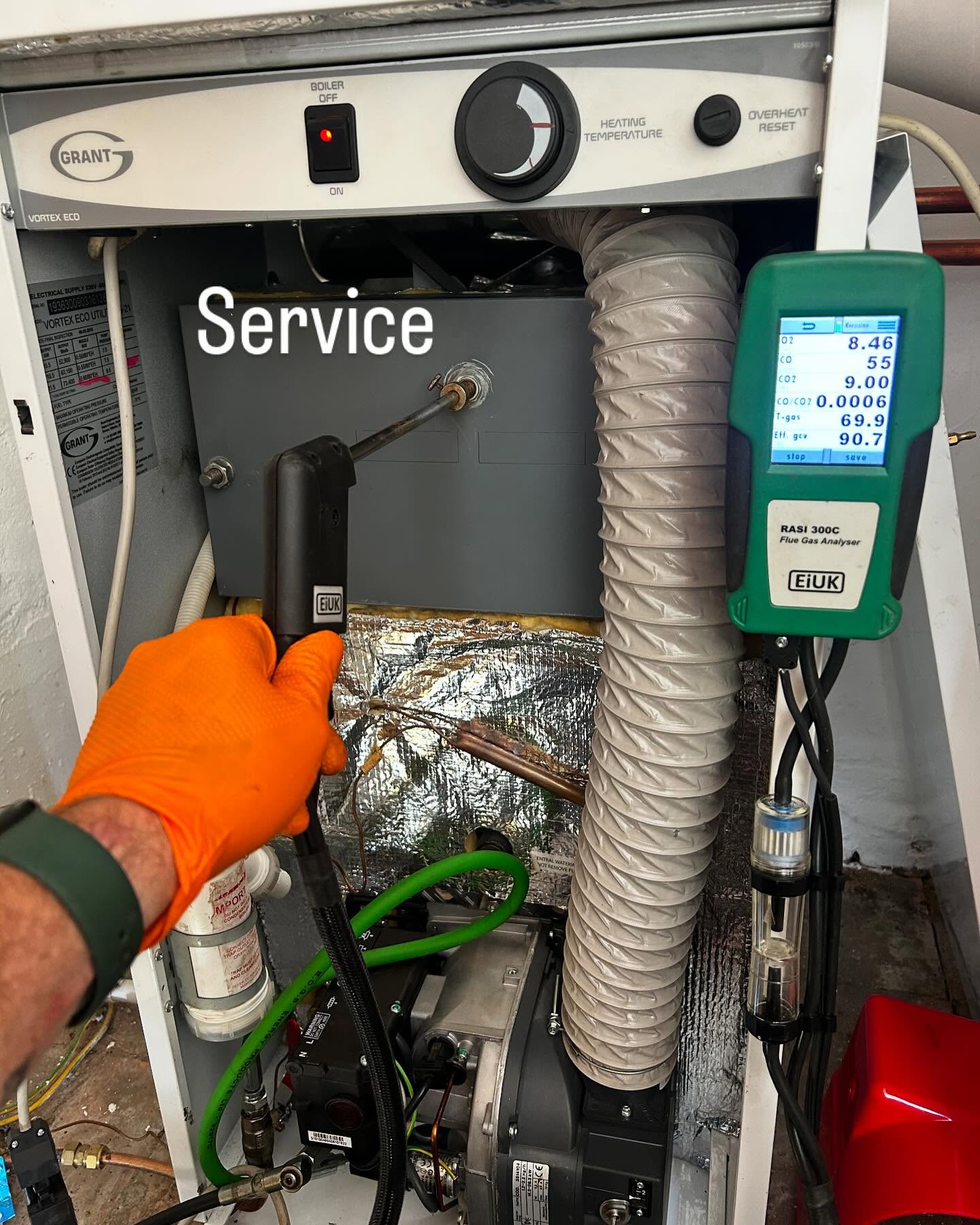 Gloved hand servicing a Grant boiler with the analyser hanging beside it