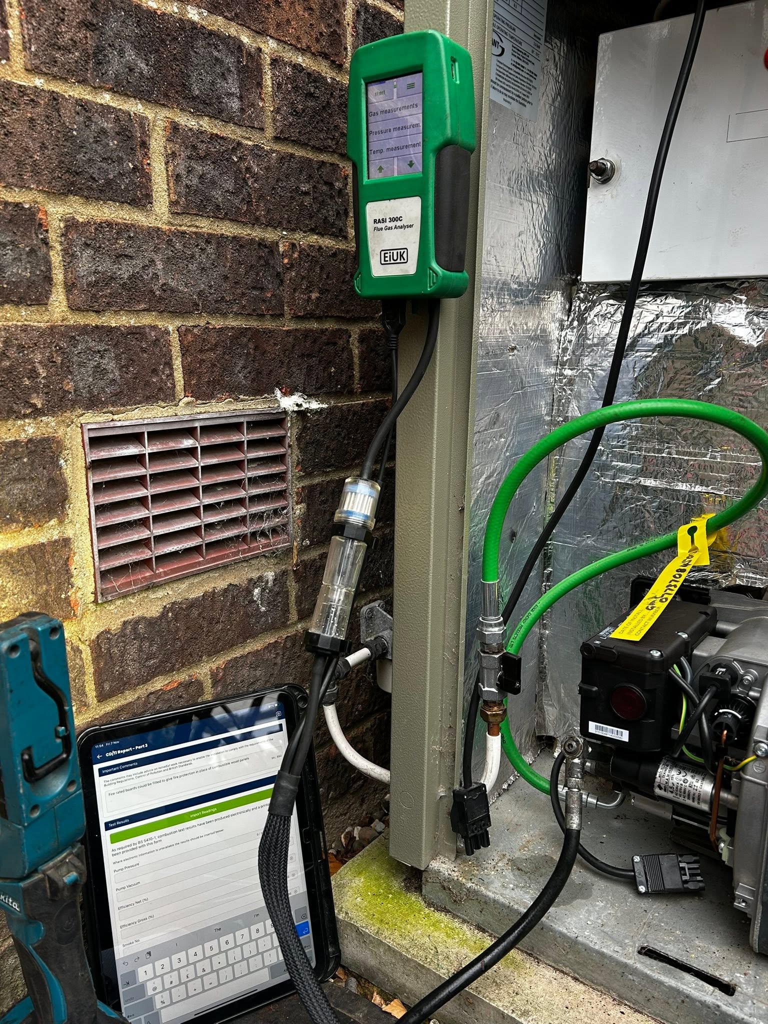 Outdoor boiler opened against a brick wall with the analyser and tablet