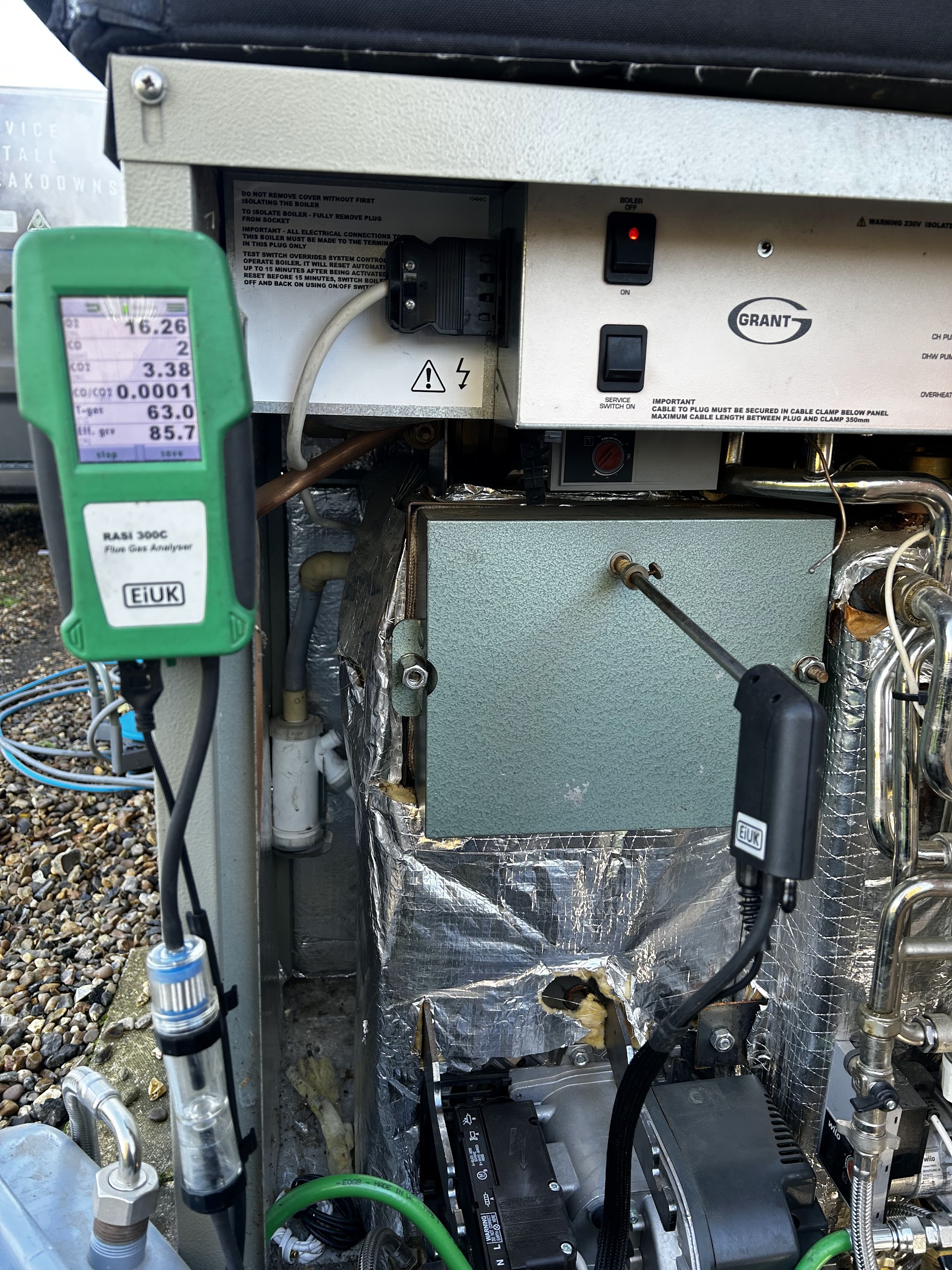 A Grant oil boiler opened up with the flue gas analyser hanging on it