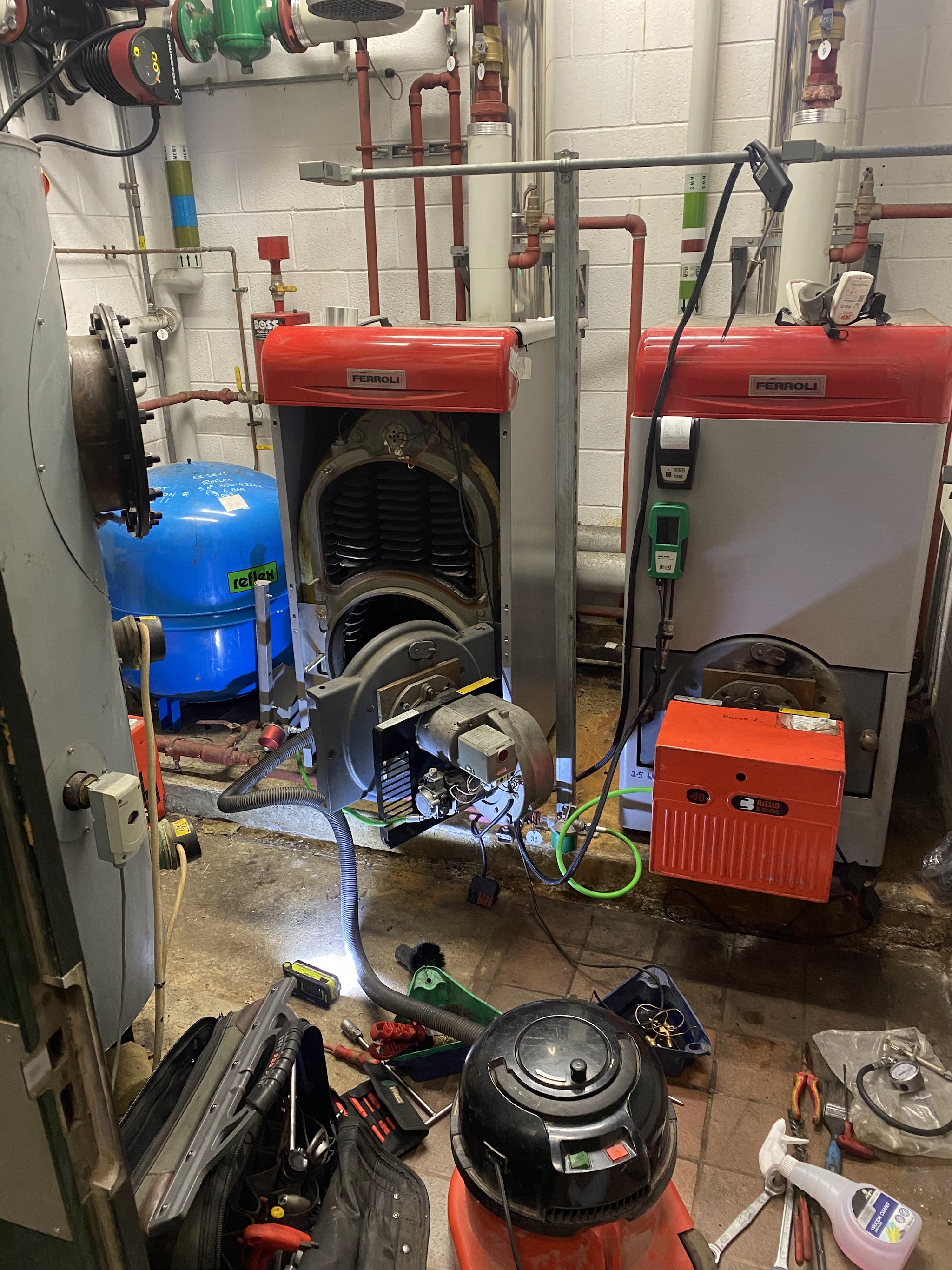 Two red oil boilers opened up in a plant room with tools on the floor